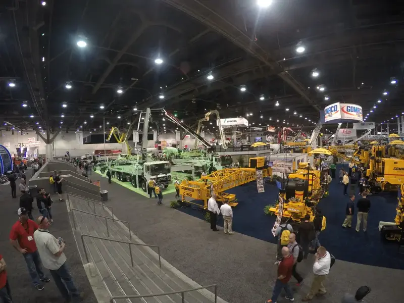 Wide view of a packed exhibit hall with concrete pumps, mixer trucks and paving machines on display