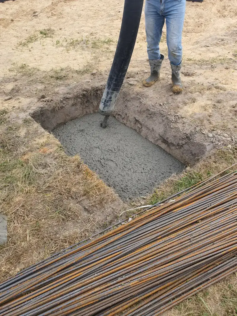 Fresh concrete poured into a foundation with rebar and a worker standing beside it