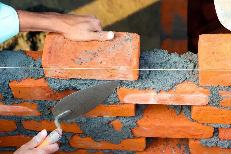 Hands laying bricks with mortar on a wall under construction
