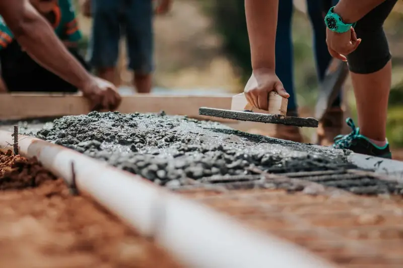 Close view of hands screeding wet concrete along a form board in warm sunlight