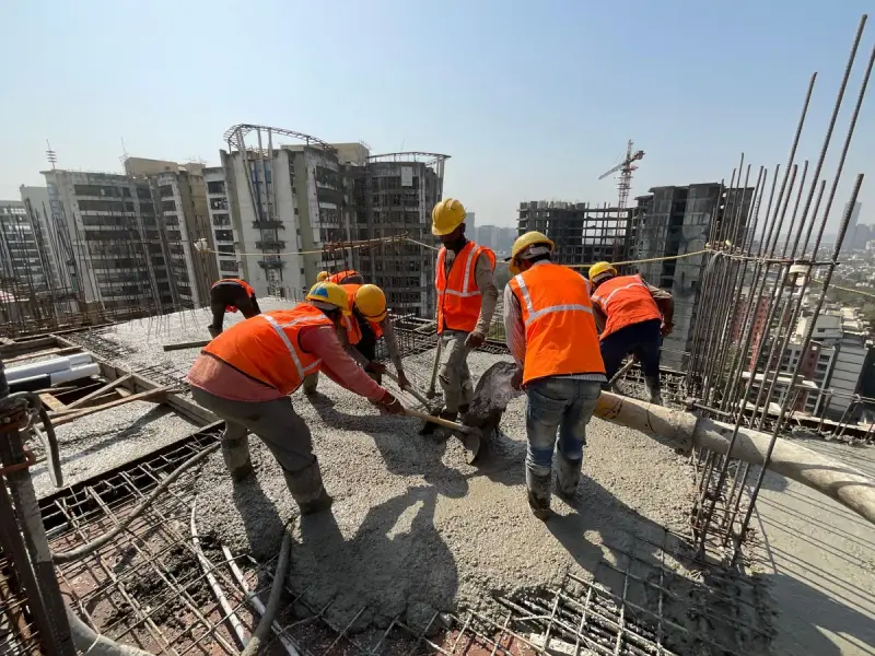Workers in orange vests and hard hats pouring and spreading concrete on a high-rise deck
