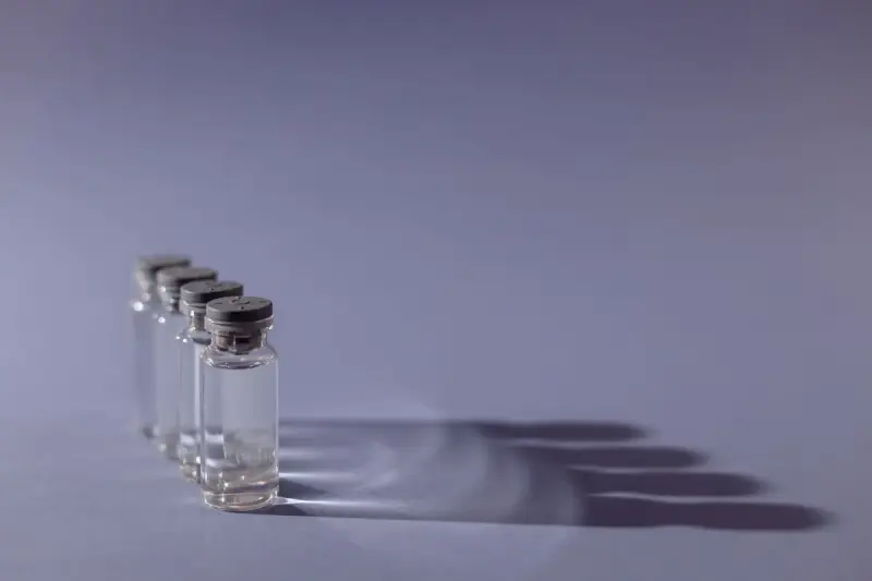 Row of small glass vaccine vials with grey stoppers casting long shadows