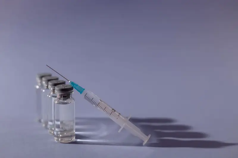 Syringe resting beside four small glass vials on a grey surface
