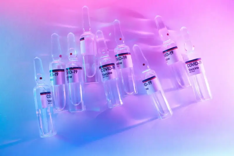 Glass vaccine ampoules scattered on a lab table under pink and blue light