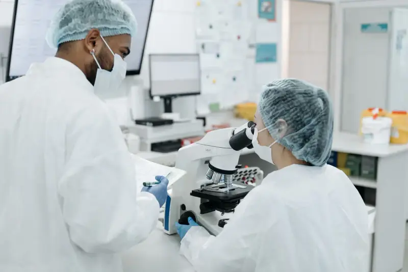 Scientist in a white protective suit and mask using a microscope