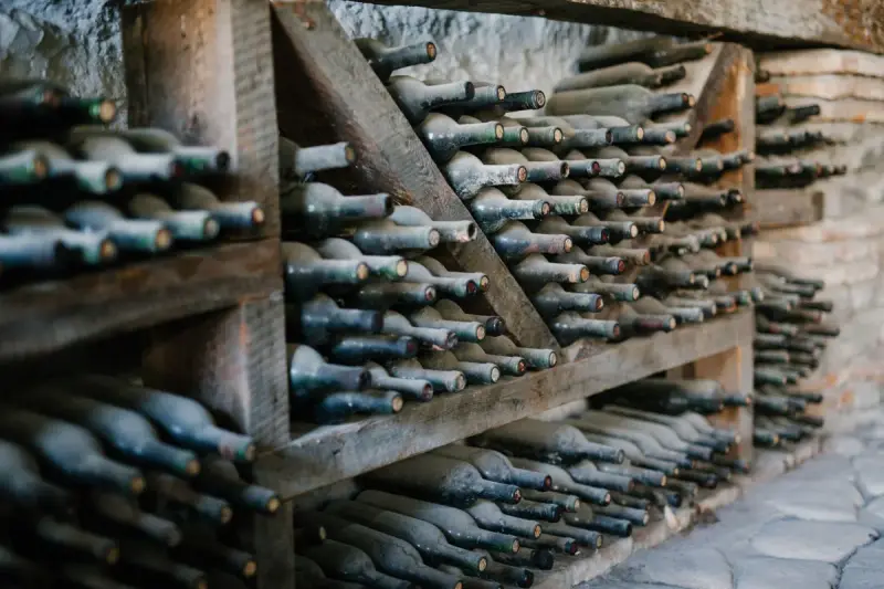 Dusty unlabeled wine bottles stacked on their sides in wooden cellar racks