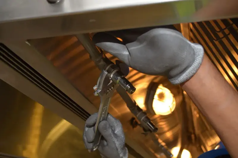 Gloved hands tightening a pipe fitting with a spanner