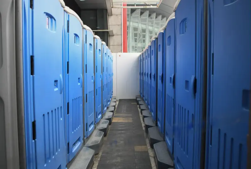 Two long rows of blue portable restrooms lined up on a construction site