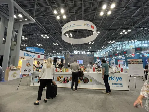 Türkiye / Turkish Tastes trade show booth built by Purple Exhibits: White Türkiye pavilion island with a circular hanging sign, white counters displaying food products and many visitors under a bright glass-roof hall.