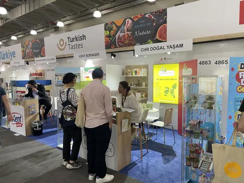 Turkish Tastes trade show booth built by Purple Exhibits: Turkish Tastes pavilion with white walls, individual exhibitor bays (Kent Boringer, CHR Dogal Yasam), food product shelves, blue carpet and visitors browsing.
