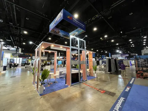 Philippine Airlines trade show booth built by Purple Exhibits: Wide corner view of the Philippine Airlines open-frame island booth with copper wood columns, overhead blue hanging sign, palm plants and blue carpet in a la