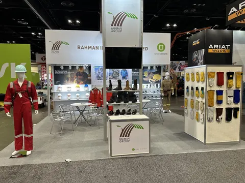 Rahman Group trade show booth built by Purple Exhibits: Rahman Group safety-workwear booth with a tall lit central tower, red coverall mannequins, wall displays of work boots and safety gloves on a white pegboard, and a