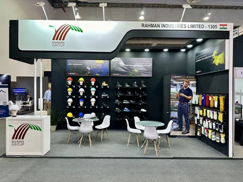 Rahman Industries Limited trade show booth built by Purple Exhibits: Rahman Group inline booth with a white curved header, dark back wall displaying safety helmets, work boots and gloves, and two round white meeting tabl