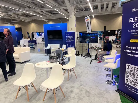 LeadSquared trade show booth built by Purple Exhibits: LeadSquared booth interior seen from the floor, with white Eames-style chairs and round tables on grey carpet, navy blue graphic walls with screens, a rollup banner