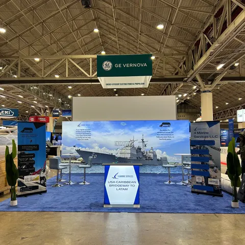 4 Marine Services LLC trade show booth built by Purple Exhibits: Clean 10x20 inline booth for 4 Marine Services with a large backlit back wall showing a US Navy warship, a white lightbox counter reading 'USA Caribbean Br
