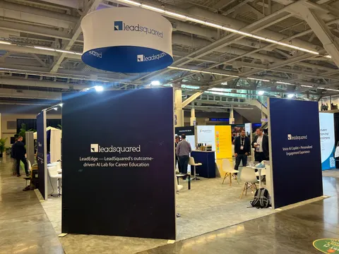 LeadSquared trade show booth built by Purple Exhibits: Navy LeadSquared island booth with a round blue-and-white hanging sign and wall graphics about an AI lab for career education, white chairs and meeting tables inside