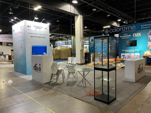 dmi digital illustrate inc. trade show booth built by Purple Exhibits: Wide view of the light blue and white dmi booth featuring a tall graphic tower, white counters, a black-framed glass display case, white chairs and a