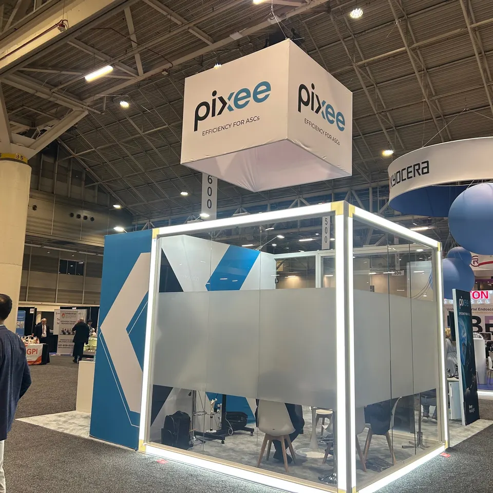 Pixee booth by Purple Exhibits: pixee 'Efficiency for ASCs' island booth with a white hanging cube sign, a reference for planning a ASHP Midyear booth