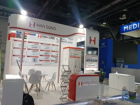 Han Song trade show booth built by Purple Exhibits: White-and-red Han Song dental milling burs booth with wall-mounted product panels, an Amazon storefront graphic, a red reception counter, a spiral brochure stand and wh