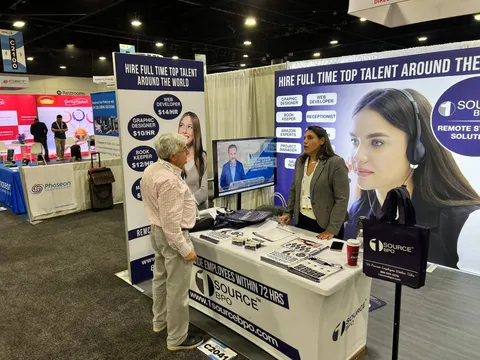 1 Source BPO trade show booth built by Purple Exhibits: Inline 1 Source BPO booth with a curved white counter, blue-and-white graphics of a headset-wearing woman, hourly-rate pricing panels and a mounted monitor, staffed