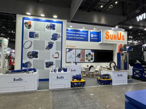 SunUs trade show booth built by Purple Exhibits: Clean white-and-blue SunUs inline booth displaying planetary gear reducers on the back wall and on white pedestals, with a large monitor, blue accent floor and a small mee