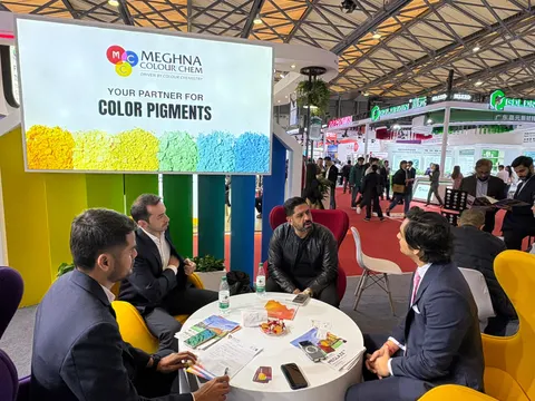 Meghna Colour Chem trade show booth built by Purple Exhibits: Meghna Colour Chem booth with a backlit colour-pigment header graphic, rainbow-striped wall panels and a white round table where four men in suits meet in col