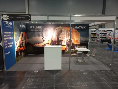 Italmix Corporation trade show booth built by Purple Exhibits: Small inline booth for Italmix with a large orange self-propelled diet feeder graphic on the back wall, a white counter and a bistro table with two chairs on