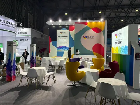 Meghna Colour Chem trade show booth built by Purple Exhibits: Wider view of the Meghna Colour Chem pigment booth with red, yellow and teal swirl graphics, yellow and purple egg chairs, round white tables, colourful spray