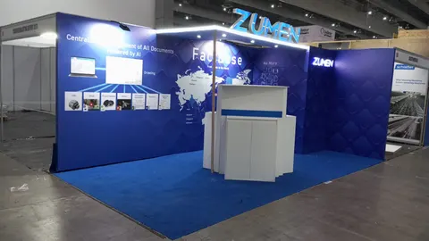 Zumen trade show booth built by Purple Exhibits: Blue inline booth for Zumen AI document management software with a world map graphic, quilted side wall, white and blue counter and blue carpet, photographed empty.