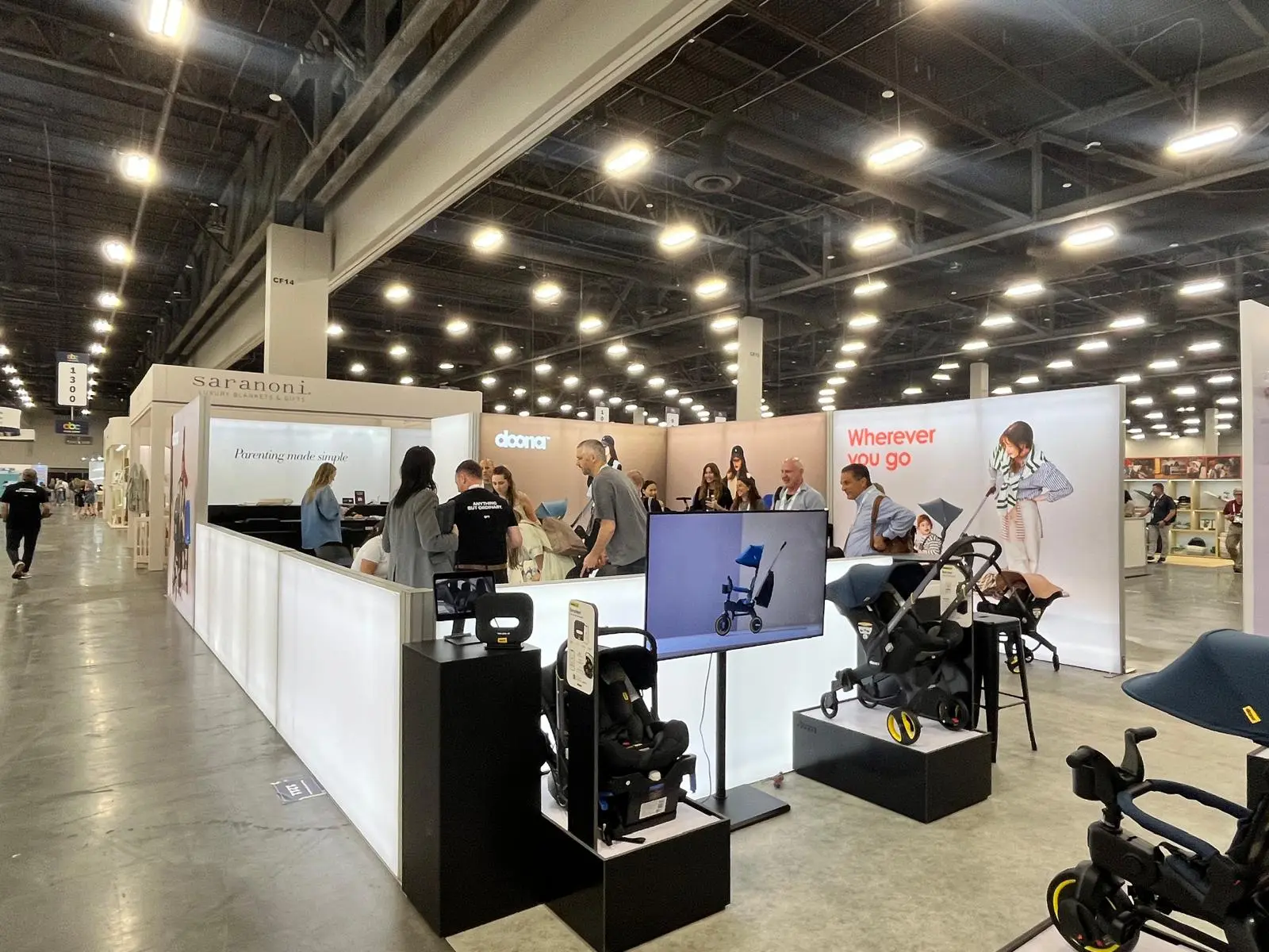 Doona booth by Purple Exhibits: doona island booth with white counters, strollers on black plinths, a screen, a reference for planning a Philadelphia Gift Show booth