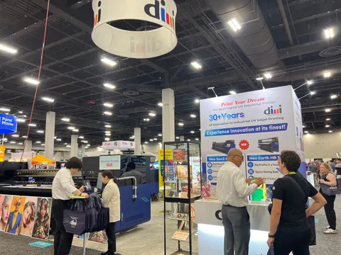 dimi trade show booth built by Purple Exhibits: dimi industrial UV inkjet printer booth with a circular white hanging sign, a tall white tower graphic promoting 30+ years, printers on display and several visitors and sta