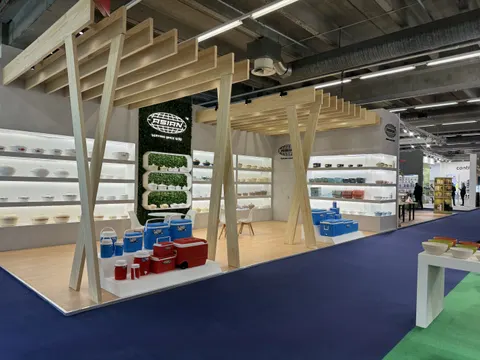 Asian trade show booth built by Purple Exhibits: Clean open booth with pale timber A-frame pergola structures, white shelving walls of bowls and containers, a green living-wall logo panel, blue coolers on display and lig