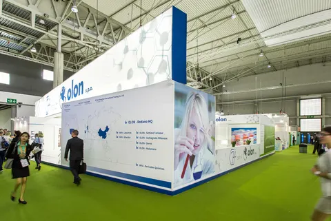 Olon S.p.A. booth by Purple Exhibits: tall white Olon pharma booth with blue accents, a world-map site graphic
