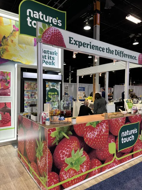 Nature's Touch trade show booth built by Purple Exhibits: Close-up of the Nature's Touch strawberry-wrapped sampling counter with 'Experience the Difference' header, glass freezer, backlit fruit graphics and snacks laid