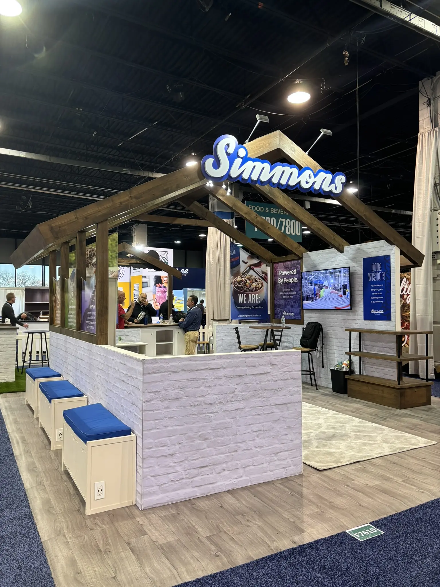 Simmons booth by Purple Exhibits: farmhouse-style open booth with dark timber roof trusses
