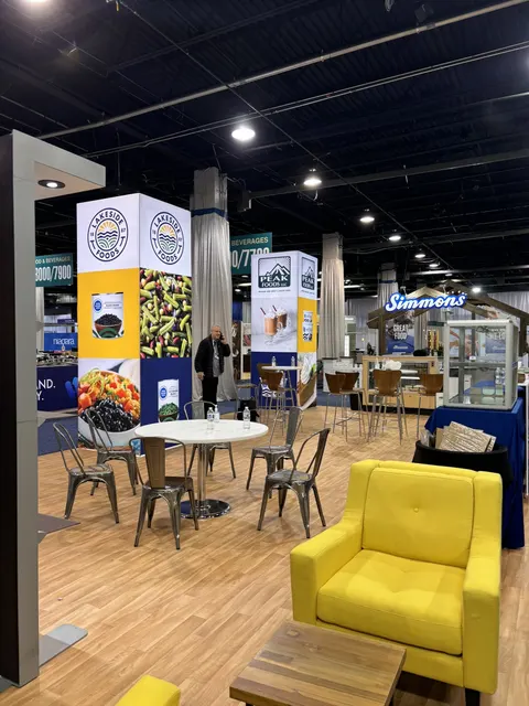 Lakeside Foods trade show booth built by Purple Exhibits: Open food pavilion with backlit Lakeside Foods and Peak Foods column towers showing vegetable and beverage imagery, cafe tables with metal chairs, wood-look floor
