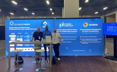 Prosperoware trade show booth built by Purple Exhibits: Blue backlit inline wall for Prosperoware, Power Desktop and Umbria with product messaging, a white counter with stools and three staff posing in front of a monitor