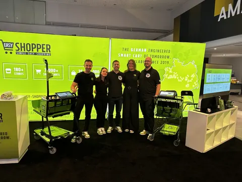 Easy Shopper trade show booth built by Purple Exhibits: Lime-green Easy Shopper backlit wall with stats graphics, smart shopping carts on display, a monitor and a white shelving unit, with five staff in black shirts posi