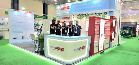 Wisepower Enterprise trade show booth built by Purple Exhibits: Finished Wisepower Enterprise booth with a light-blue header, red logo, curved white reception counter, red-and-white product shelving and staff posing on g