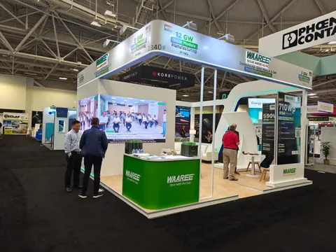 Waaree booth by Purple Exhibits: wide view of Waaree's white and green solar-module island booth with an overhead header