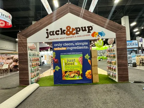 Jack&Pup trade show booth built by Purple Exhibits: Front view of the Jack&Pup booth with a dark wood-grain peaked-roof frame, white gable header, a navy central graphic promoting Just Beef Veggies treats, wood-look side