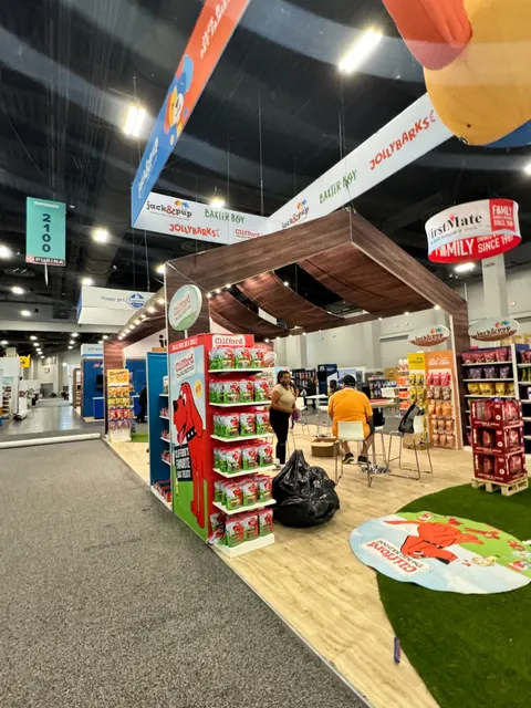 Jack & Pup trade show booth built by Purple Exhibits: Portrait view of the Jack & Pup / Clifford pet-treat island with dark wood canopy structure, red Clifford product displays, wood-look flooring and green turf, a hangi