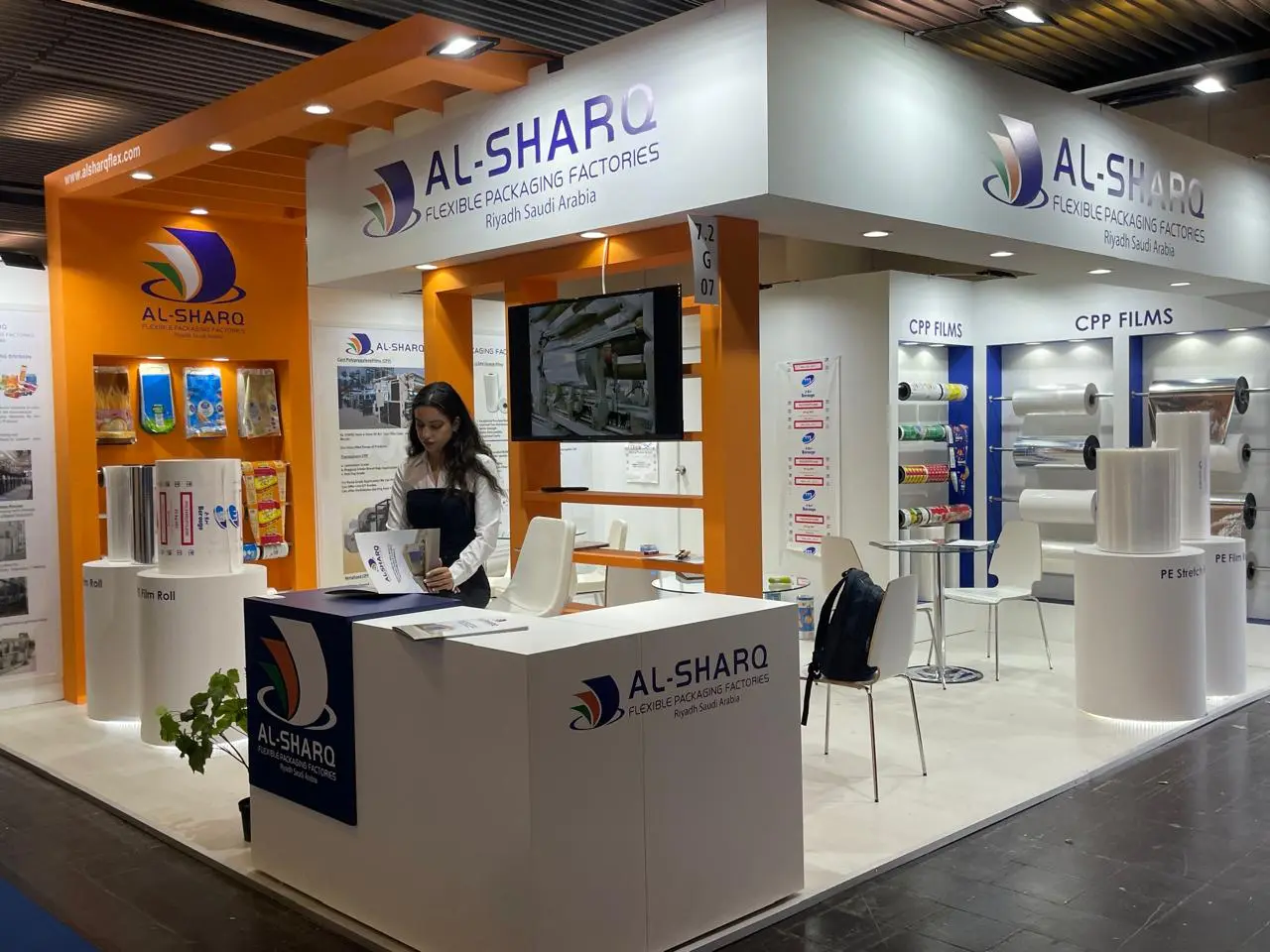 Al Sharq booth by Purple Exhibits: al Sharq packaging booth in orange and white with a blue-fronted reception counter