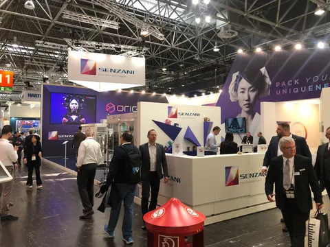 Senzani booth by Purple Exhibits: busy show-floor view of the white Senzani island booth with a hanging sign