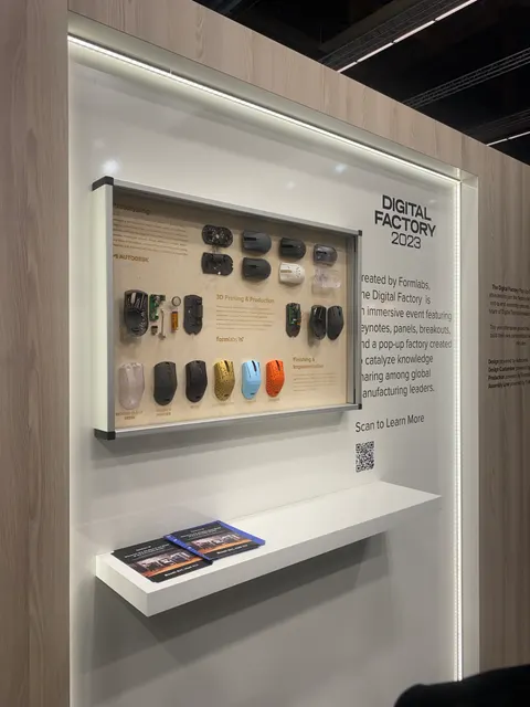 Formlabs trade show booth built by Purple Exhibits: Close-up of a light-wood wall with an edge-lit display case of 3D-printed computer mice for Formlabs Digital Factory 2023, a white shelf with brochures and a QR code.
