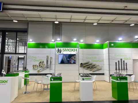 SMOXH trade show booth built by Purple Exhibits: Frontal view of the green and white SMOXH Cutting Tools booth showing the back wall with cutting tool graphics, a central screen, white pedestals and white chairs with bar