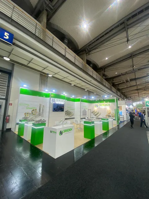 SMOXH trade show booth built by Purple Exhibits: High-angle portrait view of the green and white SMOXH booth in a hall with lots of ceiling and aisle visible, showing pedestals, graphic walls and visitors in the distance