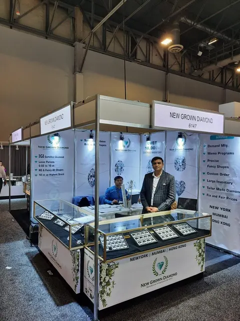 New Grown Diamond trade show booth built by Purple Exhibits: Portrait view of the New Grown Diamond corner booth with white diamond-graphic walls, a glass display case of loose diamonds and a staff member standing behind