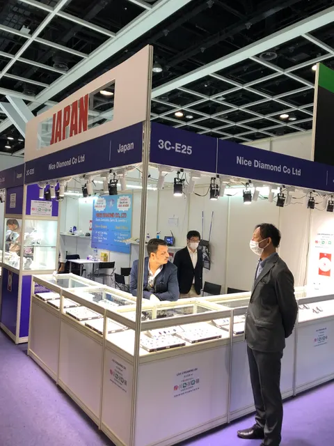 Nice Diamond Co Ltd trade show booth built by Purple Exhibits: Purple and white shell-scheme jewelry booth in a Japan pavilion with glass display counters, spotlights and a large JAPAN sign, with masked visitors and staf