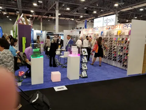 Optipak trade show booth built by Purple Exhibits: Optipak booth on blue carpet with white LED-lit pedestals, a colourful case product wall and purple accents, crowded with attendees.